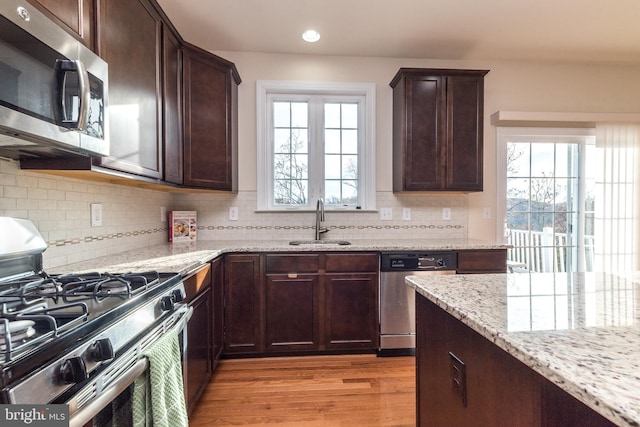 kitchen featuring sink, appliances with stainless steel finishes, light stone countertops, backsplash, and light hardwood / wood-style flooring