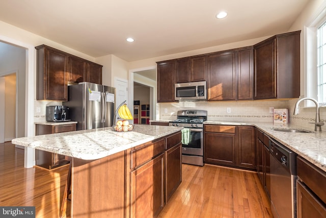 kitchen with sink, appliances with stainless steel finishes, tasteful backsplash, light hardwood / wood-style flooring, and a center island