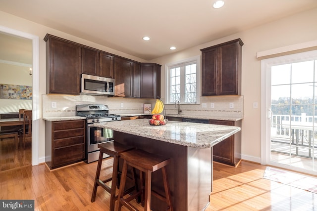 kitchen featuring stainless steel appliances, light stone counters, decorative backsplash, a kitchen island, and light wood-type flooring