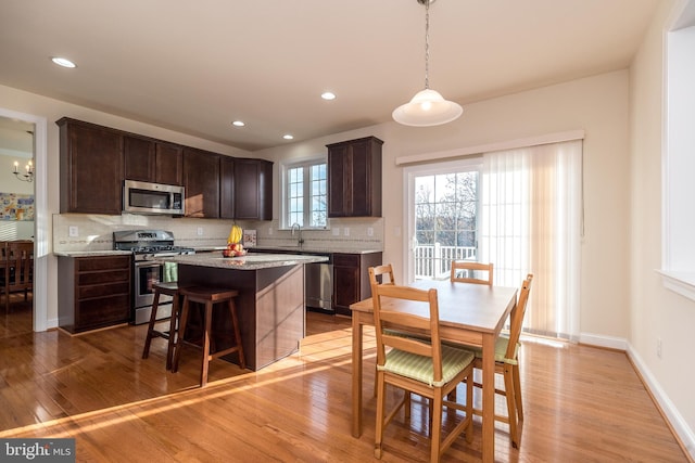 kitchen with pendant lighting, dark brown cabinets, light wood-type flooring, and appliances with stainless steel finishes