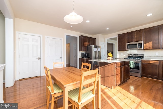 kitchen featuring light stone counters, light hardwood / wood-style flooring, hanging light fixtures, tasteful backsplash, and appliances with stainless steel finishes