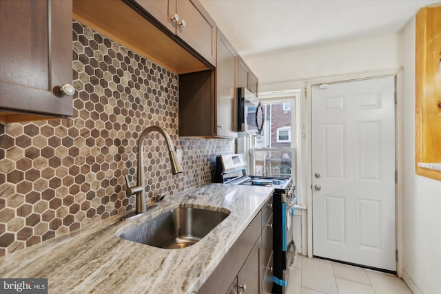 kitchen featuring backsplash, sink, light tile patterned floors, range, and light stone counters