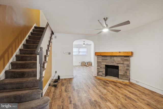 unfurnished living room featuring ceiling fan, a stone fireplace, and wood-type flooring