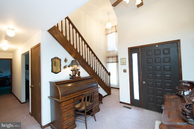 carpeted entrance foyer featuring a towering ceiling and ceiling fan