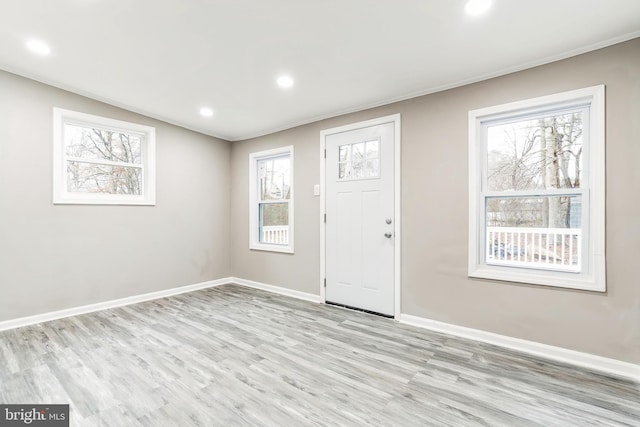 foyer entrance with crown molding, lofted ceiling, and light wood-type flooring