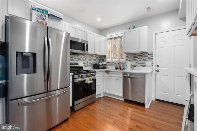 kitchen featuring white cabinets, hardwood / wood-style floors, stainless steel appliances, and tasteful backsplash