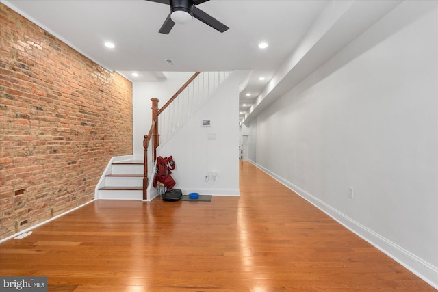 unfurnished living room with ceiling fan, light hardwood / wood-style floors, and brick wall