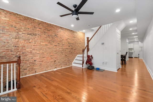 unfurnished living room with light wood-type flooring, ceiling fan, and brick wall