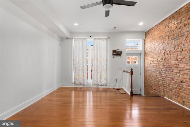 spare room with brick wall, hardwood / wood-style flooring, and ceiling fan