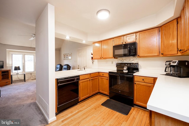 kitchen featuring vaulted ceiling, kitchen peninsula, black appliances, sink, and light hardwood / wood-style flooring