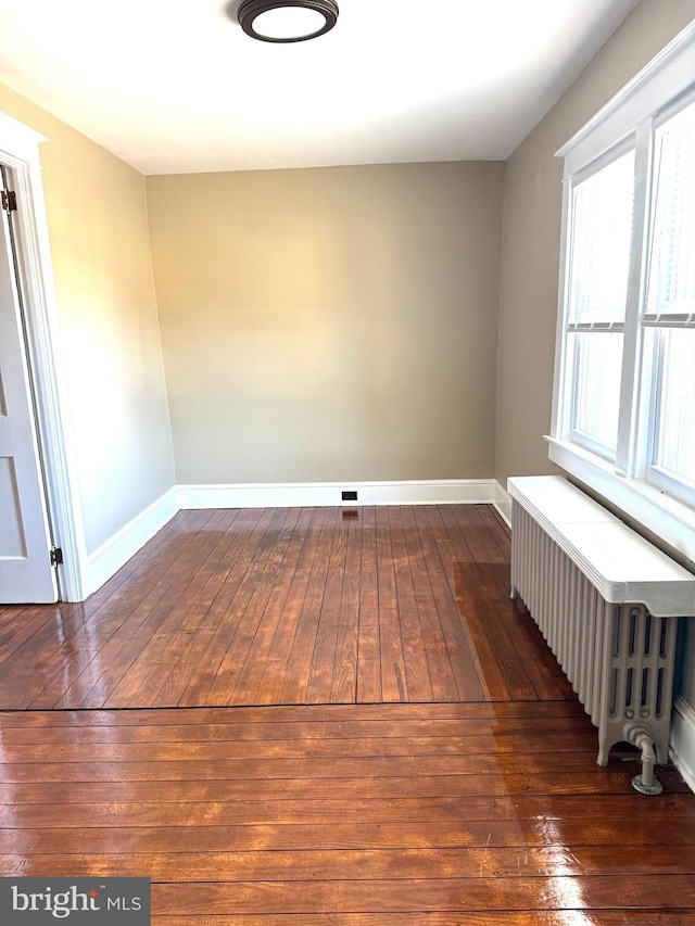 unfurnished room featuring radiator heating unit, baseboards, and dark wood-style flooring