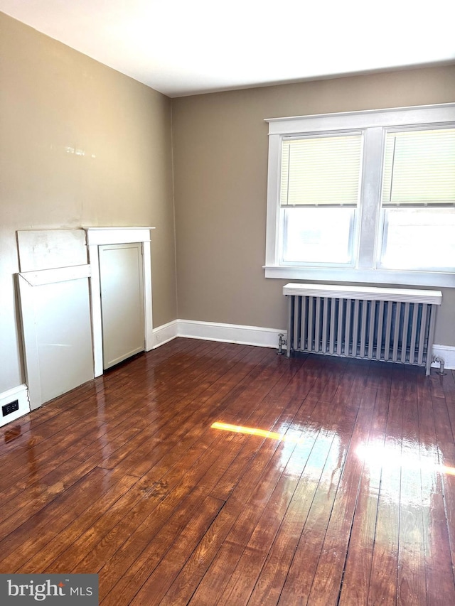 spare room with dark wood-style flooring, baseboards, and radiator heating unit