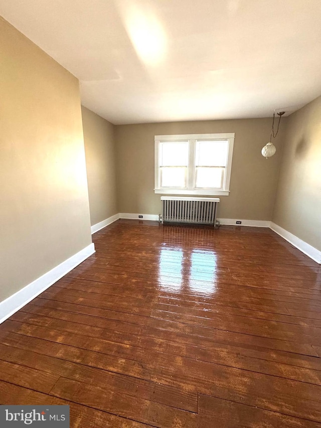 spare room featuring radiator, dark wood-style floors, and baseboards