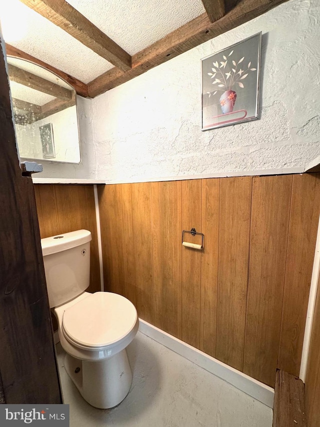 bathroom with concrete flooring, beamed ceiling, wood walls, and toilet