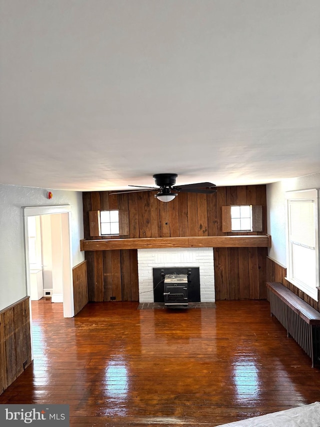 unfurnished living room with radiator, wood walls, wood-type flooring, and wainscoting