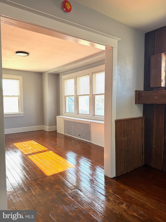 unfurnished room featuring radiator, baseboards, and dark wood-style flooring