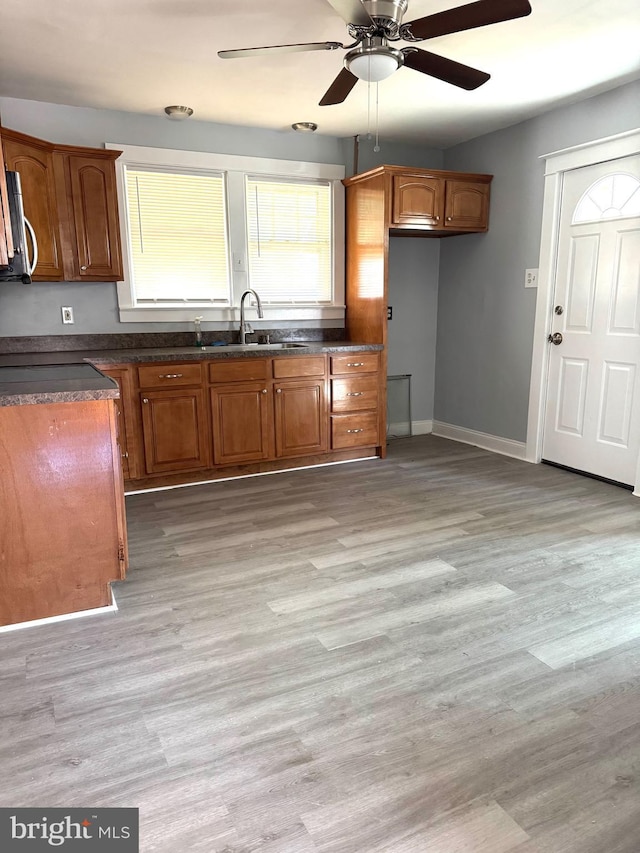 kitchen featuring brown cabinetry, dark countertops, light wood-style floors, and a sink