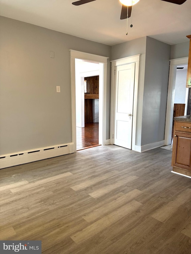 spare room with a baseboard radiator, wood finished floors, a ceiling fan, and baseboards