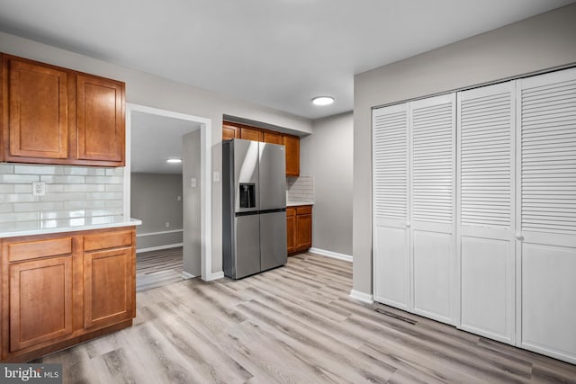 kitchen with light hardwood / wood-style floors, stainless steel fridge with ice dispenser, and tasteful backsplash