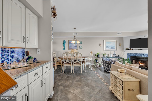 kitchen with tasteful backsplash, a tiled fireplace, decorative light fixtures, and white cabinets