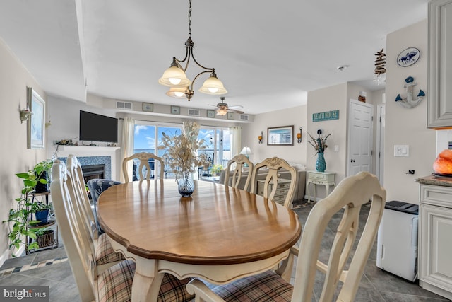 dining space with ceiling fan with notable chandelier and a fireplace