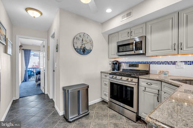 kitchen with dark tile patterned flooring, tasteful backsplash, ceiling fan, light stone countertops, and appliances with stainless steel finishes