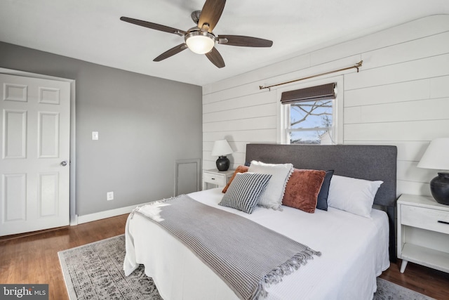 bedroom featuring ceiling fan, wood walls, and dark wood-type flooring