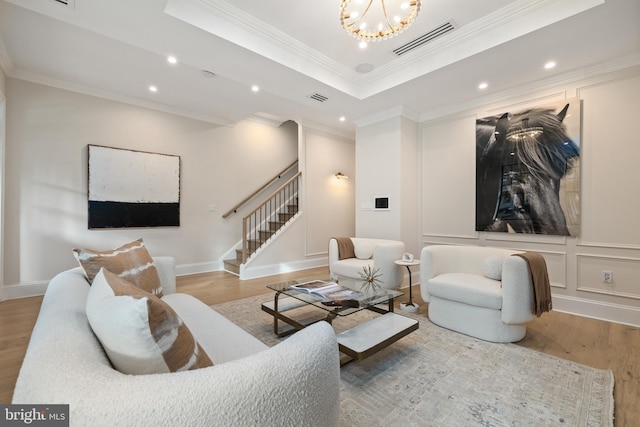 living room featuring hardwood / wood-style floors, a raised ceiling, an inviting chandelier, and ornamental molding