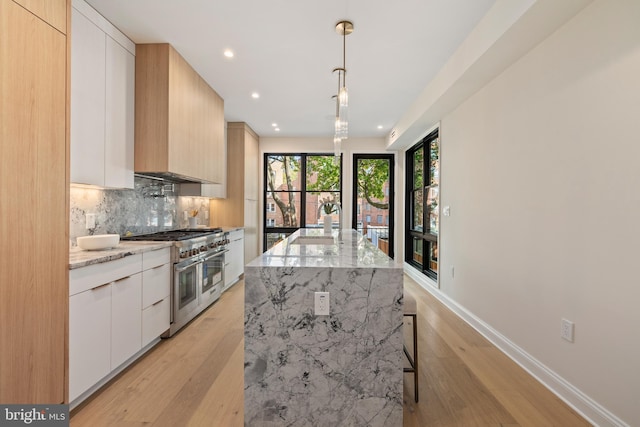 kitchen with light hardwood / wood-style floors, white cabinetry, light stone countertops, range with two ovens, and pendant lighting