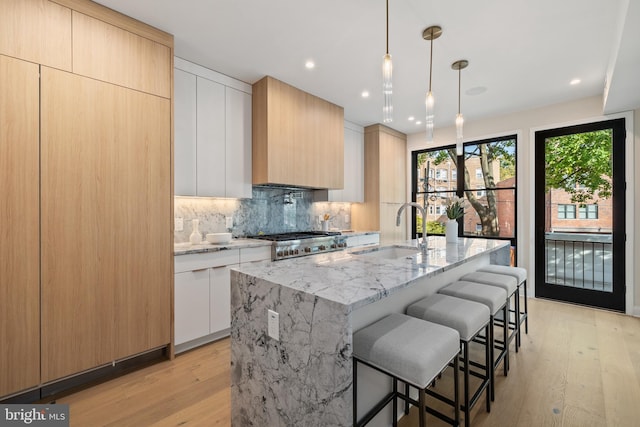 kitchen featuring a kitchen island with sink, light wood-type flooring, sink, and white cabinets