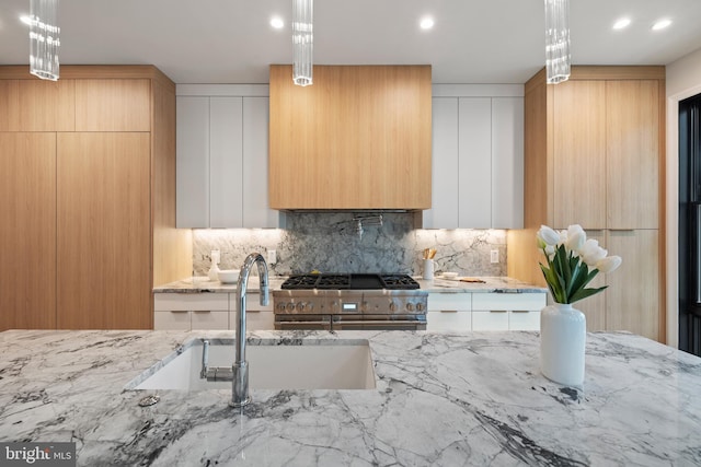 kitchen with sink, backsplash, light stone countertops, white cabinetry, and light brown cabinetry