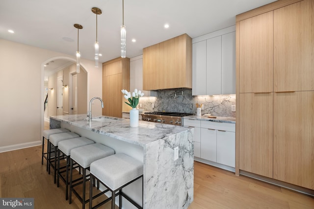 kitchen featuring white cabinetry, an island with sink, and light wood-type flooring