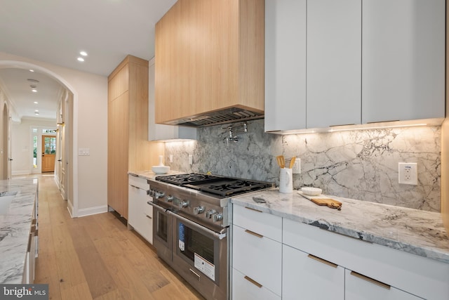 kitchen with white cabinetry, light hardwood / wood-style floors, double oven range, and light stone countertops