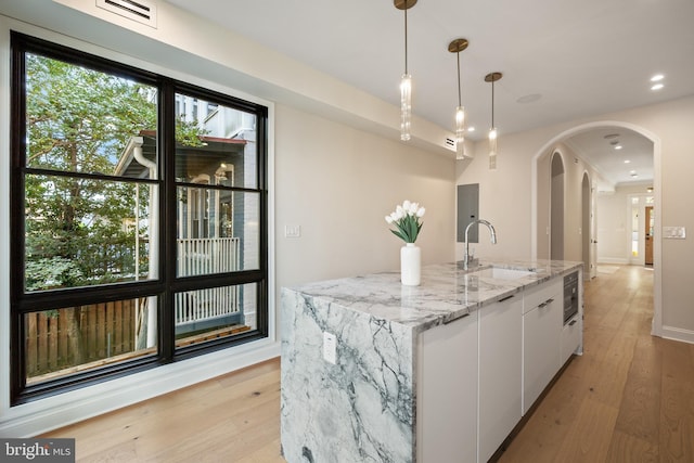 kitchen with white cabinets, sink, a kitchen island with sink, light stone countertops, and light wood-type flooring