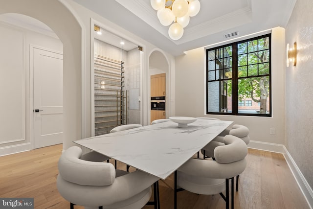 dining space with light hardwood / wood-style floors, crown molding, and an inviting chandelier