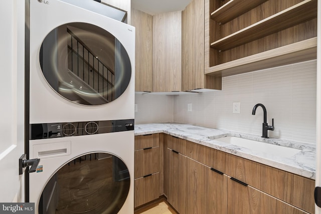 laundry room with stacked washer / drying machine, cabinets, and sink