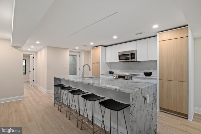 kitchen with a kitchen island with sink, white cabinets, sink, and stainless steel appliances