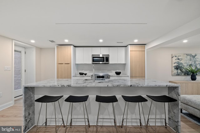 kitchen featuring white cabinetry, a large island with sink, light hardwood / wood-style flooring, and light stone counters