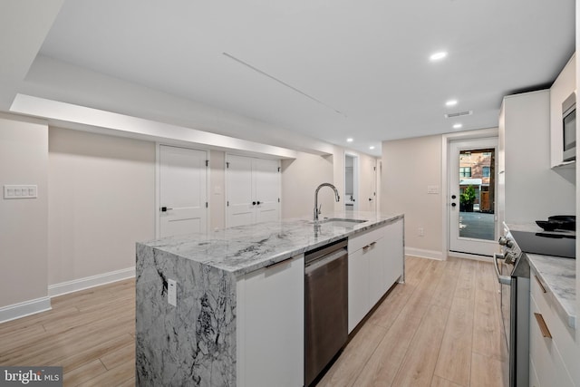 kitchen with light stone counters, stainless steel appliances, white cabinetry, light hardwood / wood-style floors, and a kitchen island with sink