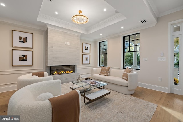 living room featuring ornamental molding, a tray ceiling, light hardwood / wood-style floors, and a fireplace