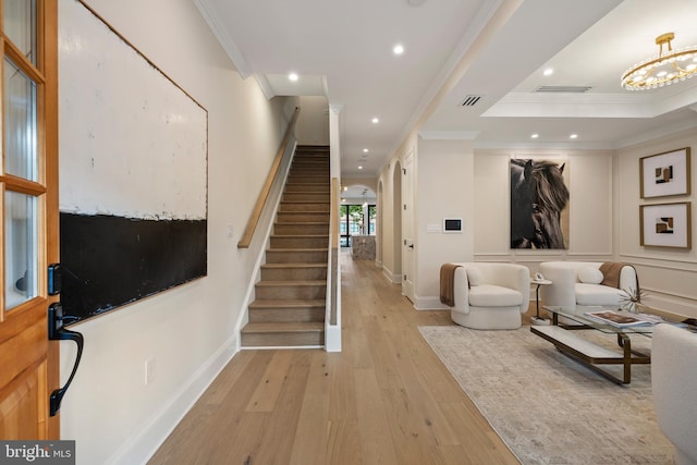 entryway featuring a chandelier, a tray ceiling, light wood-type flooring, and ornamental molding