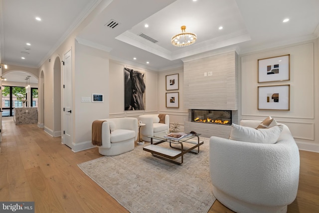 living room with ornamental molding, a tray ceiling, light hardwood / wood-style floors, and a fireplace