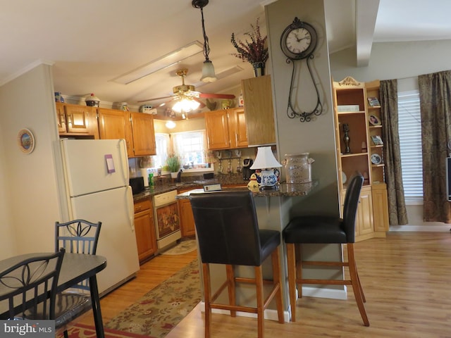 kitchen featuring light wood-type flooring, kitchen peninsula, a breakfast bar, white appliances, and ceiling fan