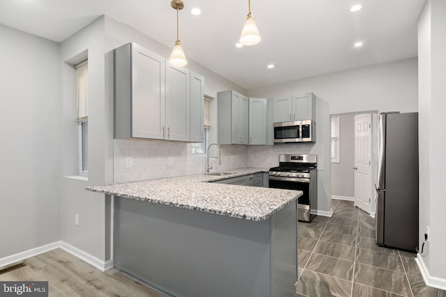 kitchen with kitchen peninsula, gray cabinetry, stainless steel appliances, sink, and pendant lighting