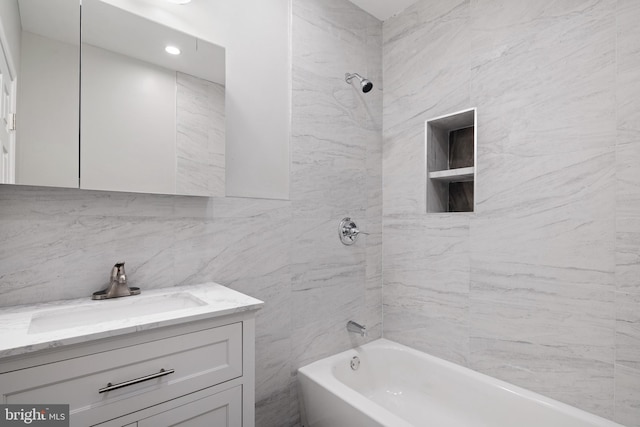 bathroom featuring vanity, tiled shower / bath, and tile walls