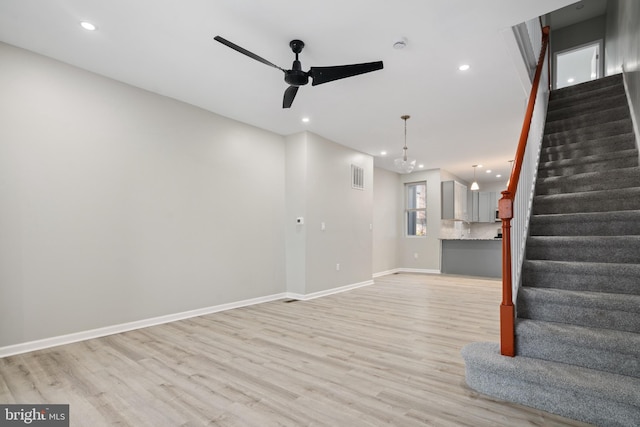 unfurnished living room with ceiling fan with notable chandelier and light wood-type flooring