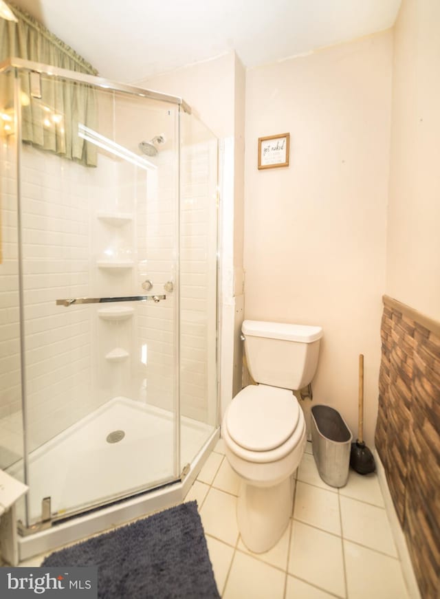 bathroom with a shower with door, toilet, and tile patterned flooring