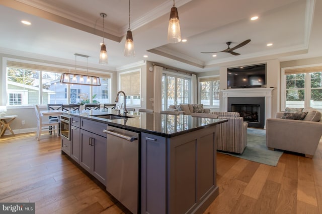 kitchen with an island with sink, sink, light wood-type flooring, and decorative light fixtures