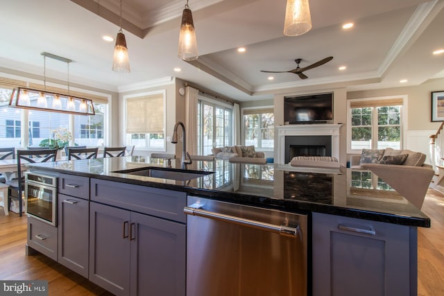 kitchen featuring a center island with sink, light wood-type flooring, stainless steel appliances, sink, and decorative light fixtures