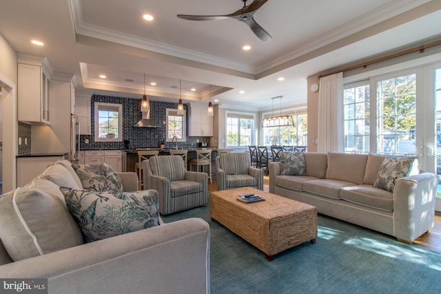 living room with ceiling fan, a raised ceiling, ornamental molding, and sink